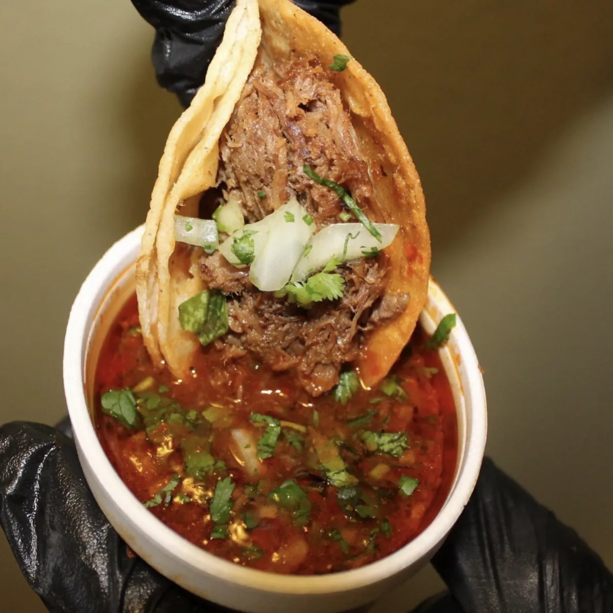 A birria taco dipped in a cup of consomé
