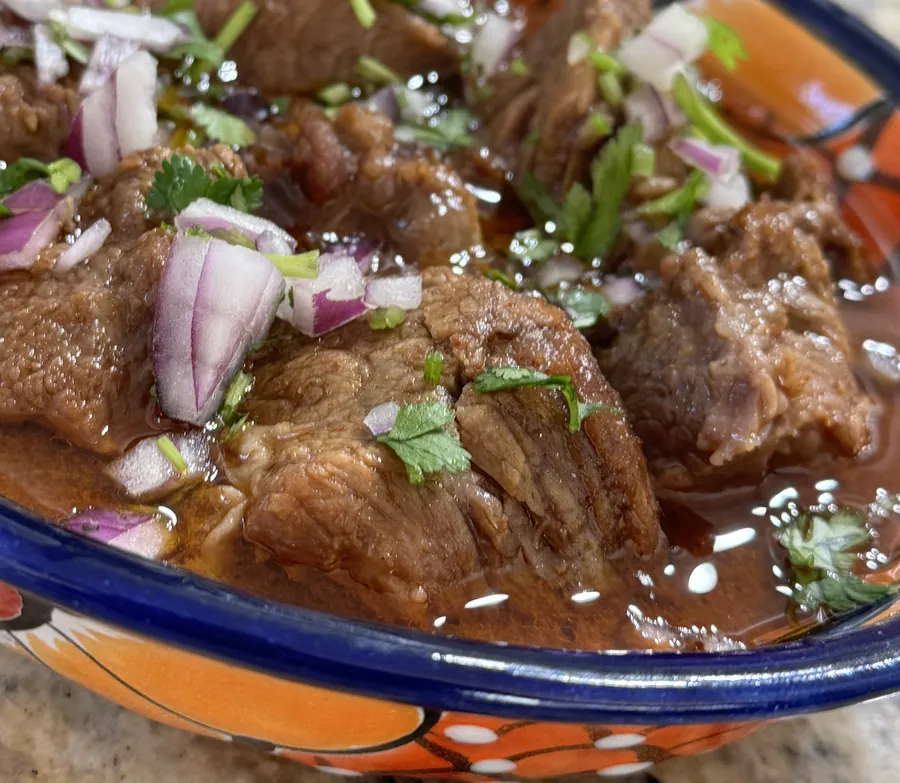 A bowl of birria with onion and cilantro